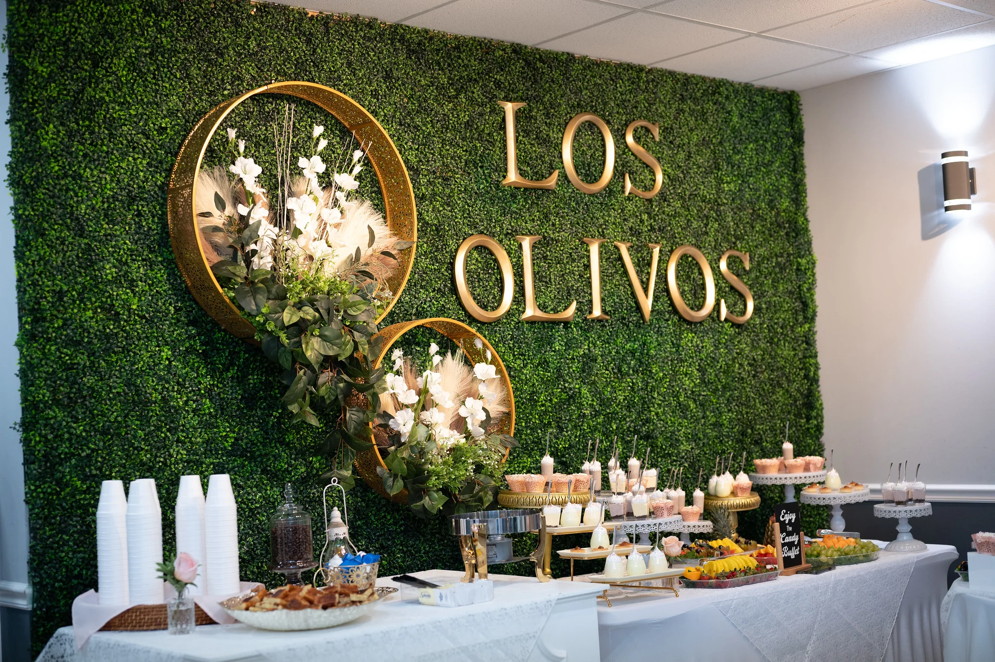 Los Olivos dessert wall with greenery, gold lettering, and buffet display