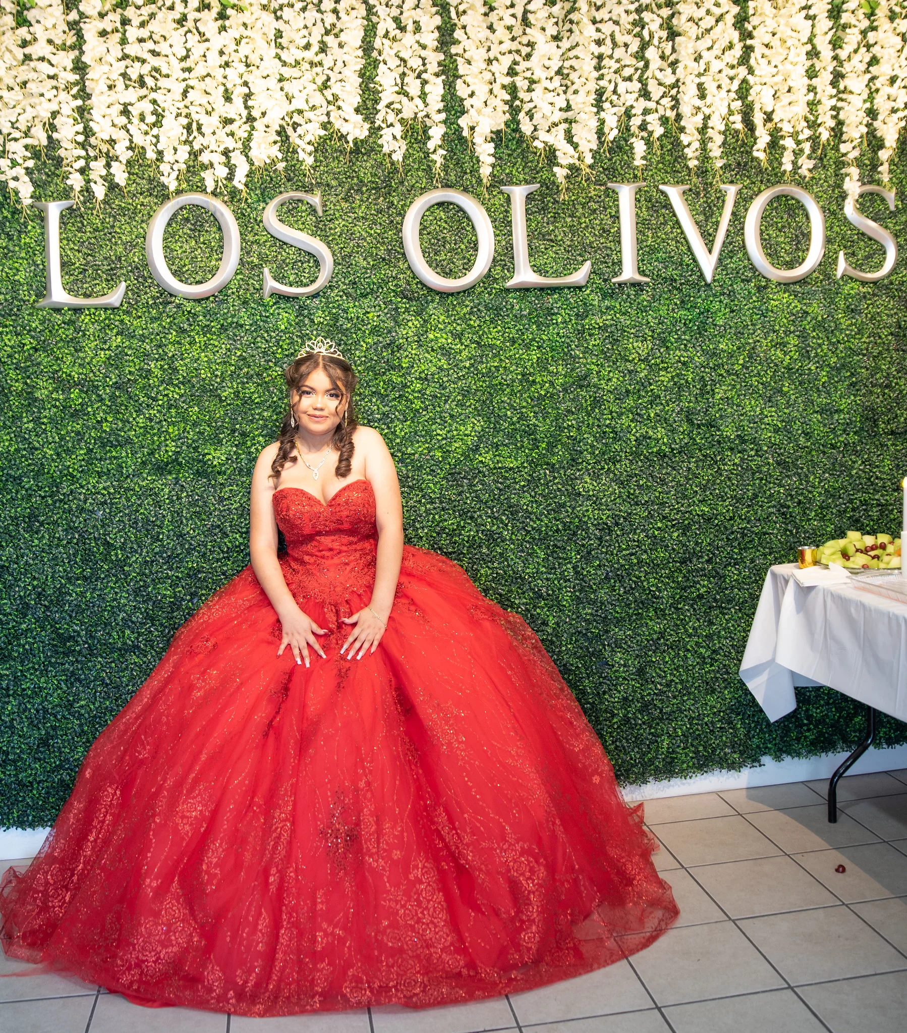 Quinceanera portrait in a red dress in front of the Los Olivos greenery wall